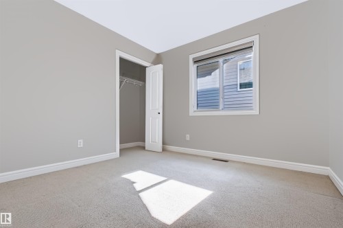 Neutral tone carpeted flooring, light grey painted walls, white trim, and a built-in closet with wire shelving - 1420 158 Street Sw, Edmonton, AB 