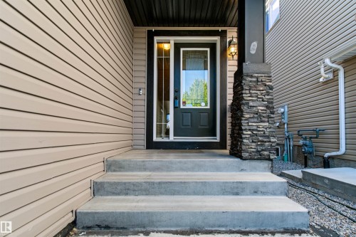 Front entry with concrete steps, a dark-paneled door, and a decorative stone-clad column - 1420 158 Street Sw, Edmonton, AB 