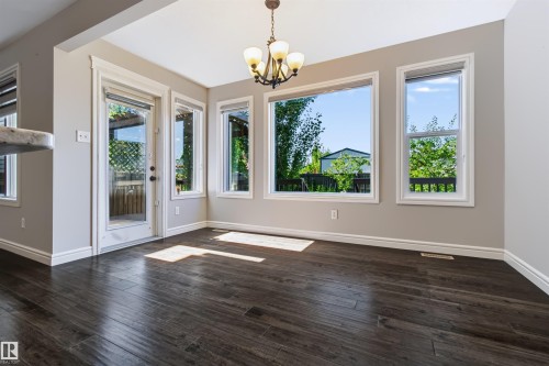 Dark wood-finish flooring, ample natural light, white trim, a glass-panel exterior door, and a multi-bulb chandelier - 1420 158 Street Sw, Edmonton, AB 