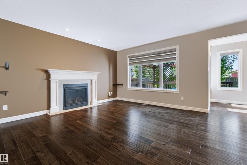 Dark wood-finish flooring, white fireplace with hearth, and large windows with privacy blinds - 1420 158 Street Sw, Edmonton, AB 