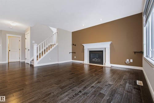 Rich wood-finish flooring, white trim, recessed lighting, a built-in fireplace with a classic mantel, and a staircase with white railings - 1420 158 Street Sw, Edmonton, AB 
