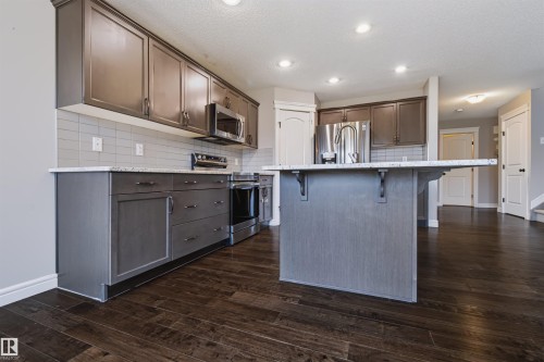 Kitchen featuring wood-finish flooring, dark-toned cabinetry, stainless steel appliances, light-toned countertops, and recessed lighting - 1420 158 Street Sw, Edmonton, AB 