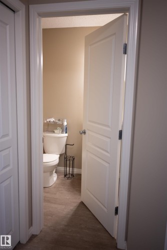 Neutral-toned wall paint with an entryway featuring a paneled door, a white toilet, and wood-finish flooring - 9014 Cooper Link Link Sw, Edmonton, AB 