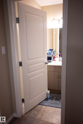 Panel interior door with hardware, wood-finish vanity with countertop and integrated sink, and overhead light fixture - 9014 Cooper Link Link Sw, Edmonton, AB 