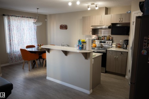 Kitchen with wood-finish flooring, light cabinetry, stainless steel appliances, and a tiled backsplash - 9014 Cooper Link Link Sw, Edmonton, AB 