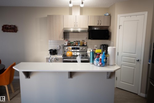 Kitchen featuring light wood-finish cabinetry, stainless steel appliances, a white tile backsplash, and a white countertop island - 9014 Cooper Link Link Sw, Edmonton, AB 
