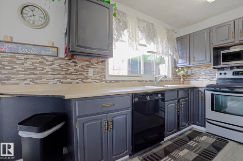 Kitchen featuring gray cabinetry, light countertops, a mosaic tile backsplash, a stainless steel range, and a built-in dishwasher - 11440 144 Avenue Nw, Edmonton, AB 