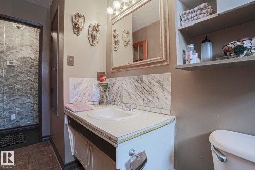 Vanity with integrated sink, stone-look backsplash, framed mirror, built-in shelving, and a tiled shower enclosure - 11440 144 Avenue Nw, Edmonton, AB 