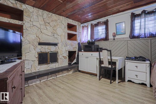 Stone-clad fireplace with integrated shelving, wood-finish flooring, wood-paneled ceiling, and wainscoting detail - 11440 144 Avenue Nw, Edmonton, AB 