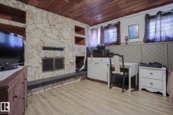 Stone-clad fireplace with integrated shelving, wood-finish flooring, wood-paneled ceiling, and wainscoting detail - 