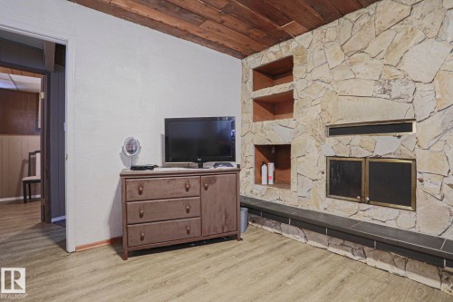 Stone-clad fireplace with a dark-toned hearth, wood-finish flooring, and a wood-paneled ceiling - 11440 144 Avenue Nw, Edmonton, AB 