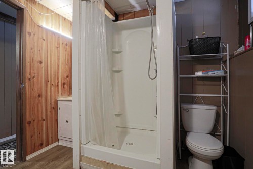 Wood-panel accent wall with overhead lighting, white shower stall with built-in shelving, white toilet, and wood-finish flooring - 11440 144 Avenue Nw, Edmonton, AB 