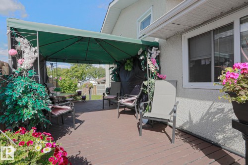 Wood-finish deck with a canopy structure, textured exterior siding, and white window frames - 11440 144 Avenue Nw, Edmonton, AB 