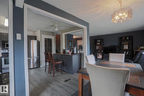 Open-concept living space with wood-finish flooring, a modern chandelier, dark cabinetry, stainless steel refrigerator, and a built-in kitchen island - 11440 144 Avenue Nw, Edmonton, AB 