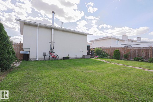 Expansive grassy yard with a stone paver pathway, mature perimeter trees, and wood fencing - 11440 144 Avenue Nw, Edmonton, AB 