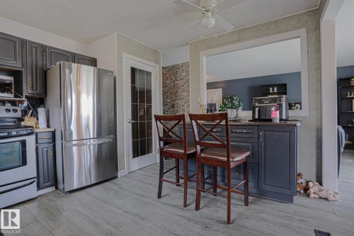 Kitchen featuring dark cabinetry, stainless steel appliances, a breakfast bar with built-in storage, and wood-finish flooring - 11440 144 Avenue Nw, Edmonton, AB 