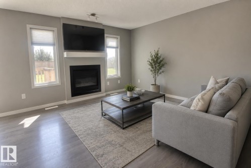 Living area featuring a sleek electric fireplace, white mantel, two large windows with roller shades, and wood-finish flooring - 4847 173 Avenue Nw, Edmonton, AB 