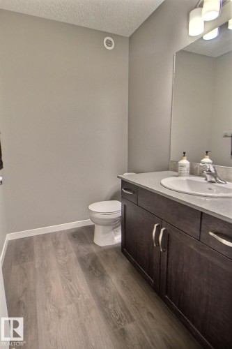Wood-finish flooring, dark wood vanity with brushed nickel hardware, integrated sink, and a wall-mounted mirror - 4847 173 Avenue Nw, Edmonton, AB 
