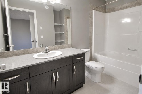 Bathroom featuring a dark wood-finish vanity with a light countertop, an integrated sink, a large wall-mounted mirror, and a shower-tub combination with tile surround - 4847 173 Avenue Nw, Edmonton, AB 