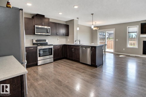 Open-concept kitchen with wood-finish flooring, stainless steel appliances, dark wood cabinetry, white countertops, and recessed lighting - 4847 173 Avenue Nw, Edmonton, AB 