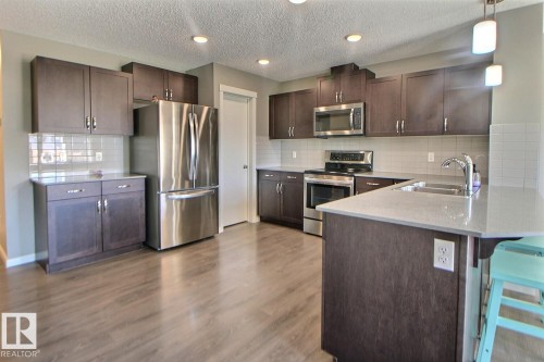 Kitchen featuring wood-finish cabinetry, stainless steel appliances, light-toned countertops, tile backsplash, and recessed lighting - 4847 173 Avenue Nw, Edmonton, AB 