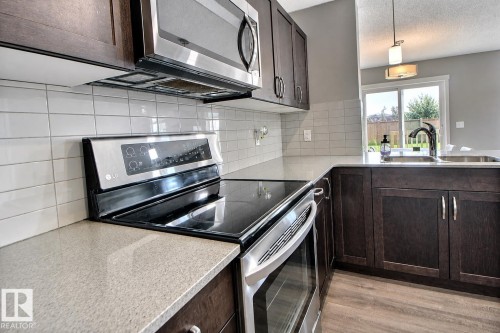 Kitchen featuring dark wood-finish cabinetry, light-toned countertops, white subway tile backsplash, and stainless steel appliances - 4847 173 Avenue Nw, Edmonton, AB 