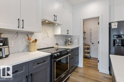 White shaker cabinetry, contrasting lower cabinetry, quartz countertops, tile backsplash, and a built-in range - 34 Raspberry Road, St. Albert, AB 