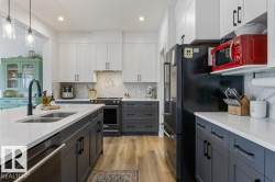 Spacious kitchen featuring an island with an undermount sink, white countertops, wood-finish flooring, and white upper cabinetry - 