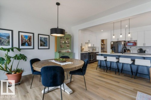 Wood-finish flooring throughout, a kitchen island with seating, pendant lighting, white upper cabinetry, and dark lower cabinetry - 34 Raspberry Road, St. Albert, AB 