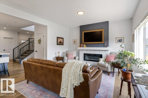 Spacious living area featuring wood-finish flooring, a contemporary fireplace with a stone-finish surround, and a prominent dark accent wall - 34 Raspberry Road, St. Albert, AB 