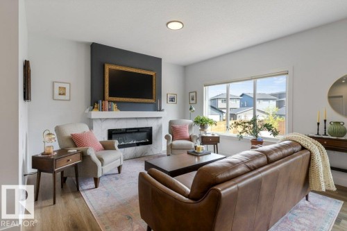 Wood-finish flooring, corner fireplace with a stone surround, large window with roller shades, and ceiling-mounted lighting - 34 Raspberry Road, St. Albert, AB 