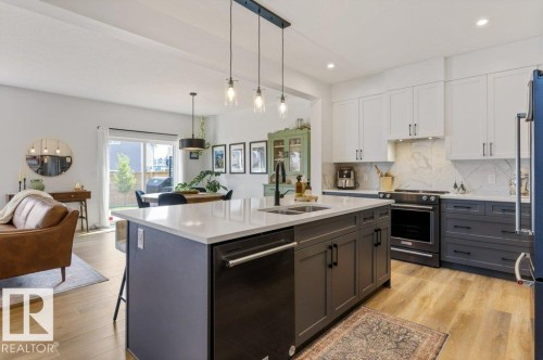 Open-concept living area featuring wood-finish flooring, a kitchen island with a built-in sink and dishwasher, white upper cabinetry, and contrasting gray lower cabinetry - 34 Raspberry Road, St. Albert, AB 
