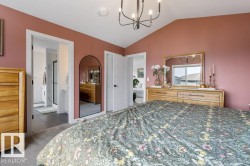Vaulted ceiling with a black chandelier, soft pink walls, wood-finish dresser with a mirror, carpeted flooring, and an adjoining bathroom with dark tile flooring - 