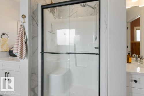 Walk-in shower with clear glass enclosure and black trim, featuring a built-in seat and a handheld showerhead - 34 Raspberry Road, St. Albert, AB 