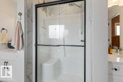 Walk-in shower with clear glass enclosure and black trim, featuring a built-in seat and a handheld showerhead - 