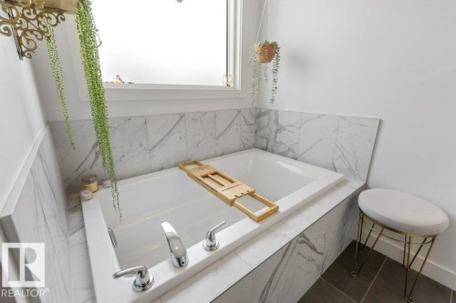 Built-in soaking tub with chrome fixtures, surrounded by white and grey veined wall tile and a white window frame - 34 Raspberry Road, St. Albert, AB 