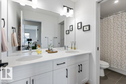 Dual undermount sinks with chrome faucets, white cabinetry featuring matte black hardware, a wide vanity mirror, and overhead vanity lighting - 34 Raspberry Road, St. Albert, AB 