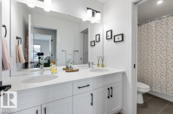 Dual undermount sinks with chrome faucets, white cabinetry featuring matte black hardware, a wide vanity mirror, and overhead vanity lighting - 