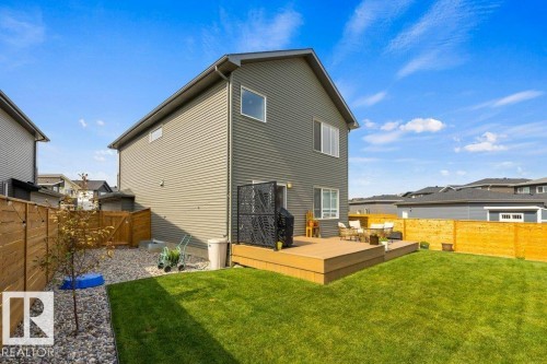Exterior siding in a neutral tone, elevated wood-finish deck, manicured lawn area, and gravel landscaping - 34 Raspberry Road, St. Albert, AB 