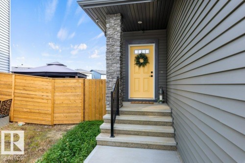 Front entrance featuring a bright yellow door, stone pillar accent, concrete steps, and a black handrail - 34 Raspberry Road, St. Albert, AB 
