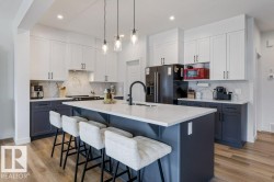 Modern kitchen with two-tone cabinetry, white countertops, a large center island, and wood-finish flooring - 