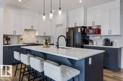 Kitchen featuring a large island with seating, two-tone cabinetry, a built-in kitchen range, and wood-finish flooring - 34 Raspberry Road, St. Albert, AB 