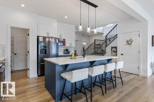 Gourmet kitchen with a large island, stainless steel refrigerator, white cabinetry, and wood-finish flooring - 34 Raspberry Road, St. Albert, AB 