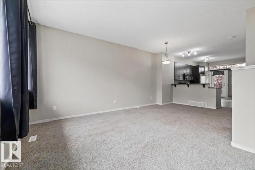 Spacious open-concept living area featuring light gray carpet flooring, neutral painted walls, and a contemporary pendant light fixture - #31 603 Watt Bv Sw, Edmonton, AB - Indoor Photo Showing Other Room