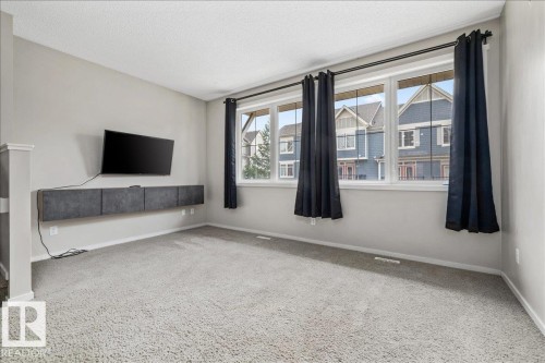 Spacious room featuring light gray walls, plush gray carpeting, and a large window array with dark drapery - #31 603 Watt Bv Sw, Edmonton, AB - Indoor