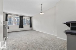 Living space featuring light gray carpeting, multiple windows with black curtain rods, and a ceiling-mounted light fixture - 