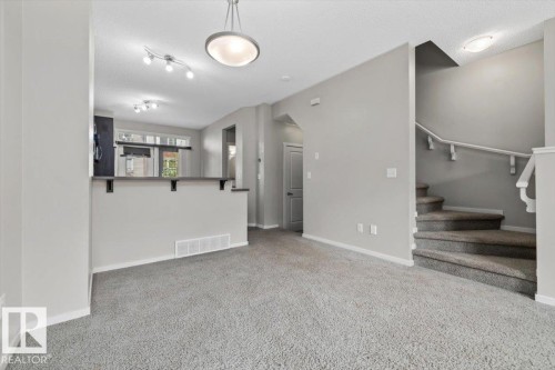 Light gray wall finishes and carpeting throughout, featuring a breakfast bar with dark countertops, a staircase with a white banister, and ceiling-mounted light fixtures - #31 603 Watt Bv Sw, Edmonton, AB - Indoor Photo Showing Other Room