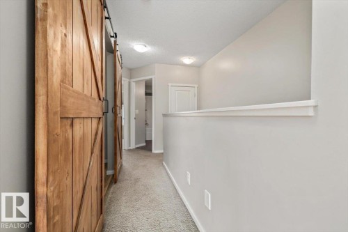Hallway featuring natural wood barn doors, neutral carpeting, recessed lighting, and light gray wall finishes - #31 603 Watt Bv Sw, Edmonton, AB - Indoor Photo Showing Other Room