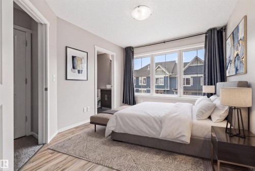 Bedroom featuring wood-finish flooring, a multi-pane window with dark drapery, and neutral wall paint - #31 603 Watt Bv Sw, Edmonton, AB - Indoor Photo Showing Bedroom