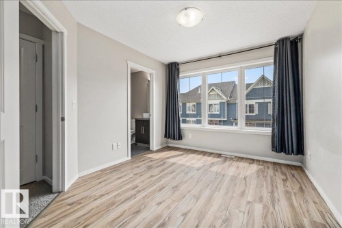 Room featuring wood-finish flooring, a three-panel window with white trim, and light gray wall paint - #31 603 Watt Bv Sw, Edmonton, AB - Indoor Photo Showing Other Room